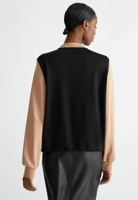 Maglione nero con maniche lunghe beige, caratterizzato da una texture morbida e una vestibilità comoda. Include polsini a costine e un collo arrotondato.