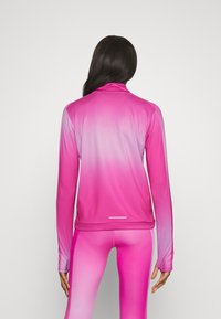 Top atletico a maniche lunghe in gradiente rosa, con colletto alto e aperture per i pollici. Realizzato in tessuto morbido ed elastico con una leggera lucentezza.