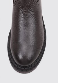 Botín de cuero negro hasta el tobillo con un acabado texturizado, puntera redondeada y suela de goma cosida. Diseño minimalista, sin logotipos ni adornos visibles.