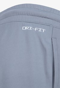 Svijetlosivi DRI-FIT materijal, glatke teksture, s ubrusom i jednim bočnim džepom. Logo otisnut u bijeloj boji.