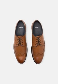 Chaussures habillées en cuir marron avec un panneau texturé, design à bouts retroussés et lacets à l'avant. La doublure intérieure est noire avec le logo de la marque. Fini lisse.
