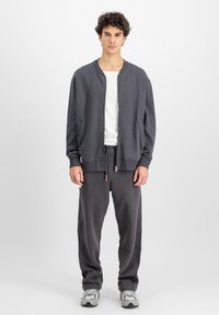 Grå zip-up bomberjacka över en vit crew neck-tröja, tillsammans med lösa grå mjukisbyxor med elastisk midja och dragsko.