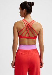 Rode sportbeha met een ingewikkeld crisscross strapdesign op de rug, gecombineerd met hoogwaist broek in roze en oranje tinten.