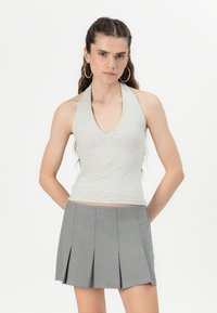 Sivý halter top s hlbokým V-výstrihom, vyrobený z mäkkej látky. V kombinácii so sivou mini sukňou so skladmi, ktorá má ostré záhyby.