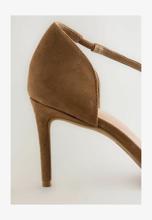 Beżowe zamszowe sandały na wysokim obcasie z ostrym noskiem, paskiem wokół kostki i smukłym obcasem typu stiletto. Gładka tekstura i prosty design.