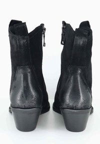 Un paio di stivali alla caviglia in suede nero con cerniere laterali, tacco impilato e linguette per il collo, mostrati dal retro su una superficie bianca.