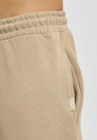 Beige sweatpants van een zachte katoenmix, met een elastische tailleband, zijzak en een klein wit logo etiket.