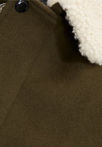 Tessuto in misto lana verde oliva con un morbido colletto in shearling di colore crema e un accento in bottone nero. Texture liscia e cuciture pulite.
