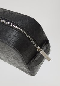 Black leather cosmetic bag featuring an embossed pattern, silver zipper, and a metal tag with "Calvin Klein" logo. Rectangular shape with rounded edges.