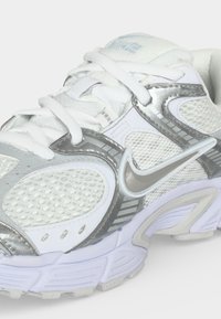 Άσπρο και ασημί αθλητικό παπούτσι Nike με διχτυωτό πάνω μέρος, παχιά σόλα και λευκά κορδόνια, φαίνεται από μπροστινή πλάγια γωνία.