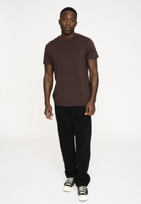 Brun kortærmet t-shirt parret med sorte bukser og sorte høj-top sneakers. Glat stoftekstur, afslappet pasform og enkelt design.