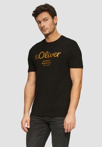 Černé bavlněné tričko s kulatým výstřihem, s textem zlaté barvy "s.Oliver Elevated Essentials Since 1969." Krátké rukávy.