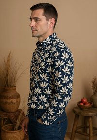 Marineblauwe blouse met knoopsluiting en een wit bloemenpatroon, lange mouwen, en een puntkraag, gecombineerd met donkerblauwe jeans.