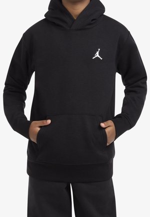 Sweat à capuche noir avec poche avant porté par une personne, arborant un logo Jumpman blanc sur le côté gauche supérieur de la poitrine.
