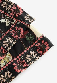 Tessuto nero con motivi floreali in tonalità di rosa, crema e verde. Texture morbida, parzialmente piegata, che rivela uno strato interno a contrasto.
