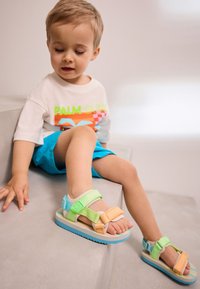 Sandali colorati per bambini con cinturini regolabili in verde, arancione e blu, suola imbottita e plantare testurizzato.