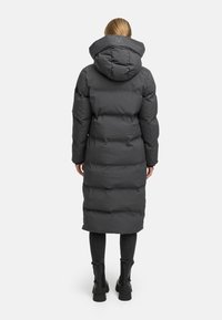 Long, puffy, dark gray down coat with a hood, featuring stitched sections for insulation. Worn over black pants and ankle boots.