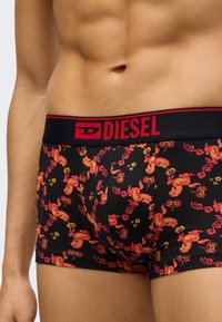 Svarte boxerbriefs med et rødt blomstertrykk, med en svart elastisk midjebånd med rød "DIESEL"-logo øverst. Mykt bomullsmateriale.