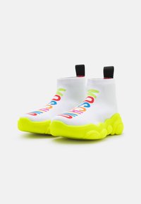 Bílé tenisky ve stylu ponožek s barevným textovým designem, limetkově zelenou gumovou podešví, texturovanou tkaninou a černými poutky na kotnících.