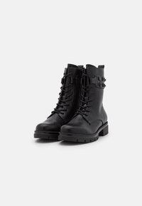 Botas de tobillo de cuero negro con diseño de cordones, suela de goma plana y acentos de hardware en los laterales. Textura suave y construcción resistente.