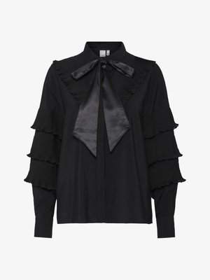 Svart bluse med lange ermer, plisserte volangkant på kragen og ermene. Har satengsløyfe rundt halsen og knappestolpe foran.