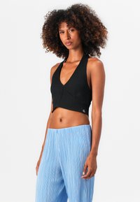 Top court noir à bretelle avec un décolleté en V profond et un ourlet évasé. Associé à un pantalon large plissé bleu clair. Détail de logo subtil.