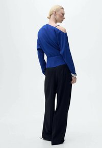 Maglione blu off-the-shoulder in un filo tessuto, abbinato a pantaloni neri a gamba larga. Presenta maniche lunghe e una vita aderente.