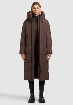 Brown long puffer coat with a hood, featuring a stitched pattern, front zipper, and side pockets. Worn over a black turtleneck and pants.