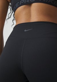 Czarne legginsy Nike z wysokim stanem, rozciągliwego materiału i niewielkim logo, zaprojektowane do użytku sportowego.