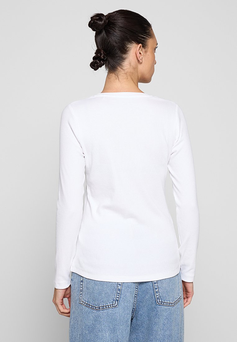 Haut à manches longues blanc avec un col arrondi, en tissu doux. Le dos présente un design minimaliste et est assorti avec un jean bleu clair.