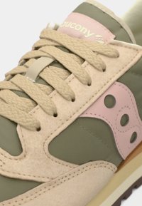 Green and beige sneaker featuring a suede and synthetic upper, textured laces, pink accents, and a distinct logo on the side panel.