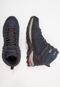Mid-Cut-Wanderstiefel mit einem Obermaterial aus blauen Wildleder und Mesh, Gummikappe, roten Akzenten und einer strukturierten schwarzen Sohle mit Profil.