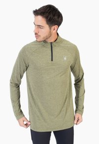 Camisa de manga larga verde con cremallera de un cuarto, fabricada con tejido texturizado y un logo en el pecho. Presenta mangas raglán y dobladillo recto.