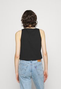 Schwarzes ärmelloses Crop-Top mit rundem Ausschnitt, kombiniert mit hoch taillierten hellblauen Jeans, die Gesäßtaschen und sichtbare Nähte aufweisen.