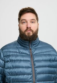 Paminkštinta žalia striukė su aukštu apykakle, pilnu užtrauktuku, pagaminta su kontrastinga apdaila ir su siuvinėta tekstūra visame kūne.
