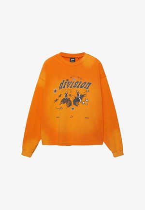 Fényes narancssárga hosszú ujjú pulóver fekete grafikai ábrával, amelyen két cowboy bika hátán lovagol, csillagok veszik körül, és a mellkason "The division" felirat olvasható.