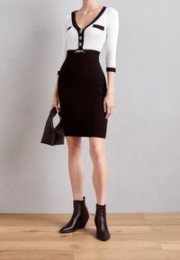Svart och vit klänning med en figursydd silhuett, knäppning framtill och bröstfickor. Betonas med en metallsnörning. Svarta anklar boots ochhandväska.