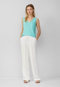 Een licht turquoise mouwloze top met een v-hals in combinatie met losse witte linnen broeken. De outfit heeft een casual ontwerp en een zachte textuur.