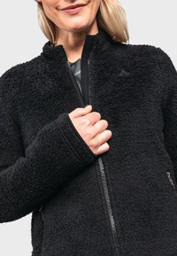 Schwarze Fleecejacke mit strukturierter Außenseite, Reißverschluss, hohem Kragen und kontrastfarbigen Akzenten. Verstellbare Bündchen und seitliche Reißverschlusstaschen sind sichtbar.