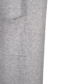 Grå stickad tyg med en mjuk struktur, med en ficka på sidan. Designen är enkel och följer kroppen.