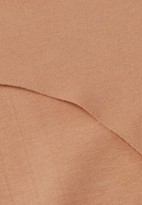 Perzikkleurige stof met een gladde, textuurrijke oppervlakte; plooien vallen zachtjes, waardoor een dunne, lichte weefsel zichtbaar wordt.