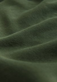 Primo piano di tessuto liscio verde scuro che mostra una sottile trama a maglia e pieghe morbide.