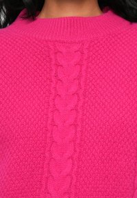 Un pull fuchsia avec un motif de tricot texturé et un détail en câble central courant verticalement. Le col côtelé ajoute du contraste au design.