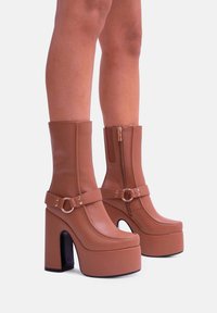 Stivaletti alla caviglia di colore beige con tacco alto a blocco, dotati di zip laterale, cinturino con fibbia e superficie liscia simile alla pelle.