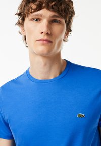 Blå bomulds T-shirt med rund halsudskæring, korte ærmer og et lille broderet logo på brystet. Glat tekstur og afslappet pasform.