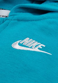 Türkoosi sviiter kangas peene tekstuuriga, mille esiosas on silmatorkavalt tikitud valge Nike logo.