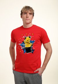 Rød bomulds T-shirt med et tegneserie-bjørn, der popper op af en sort tryllehat, prydet med farverige stjerneaccentuer og teksten "IZZY-WIZZY LAD OS KOMME I GANG!"