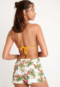 Bikini-Oberteil mit orangefarbenem Bindeband, kombiniert mit weißen Shorts mit einem bunten, tropisch-blumigen Muster. Weicher Stoff mit lockerer Passform.