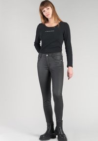 Maglietta nera a maniche lunghe con scollatura quadrata e testo bianco, abbinata a jeans neri slim-fit e stivaletti neri.