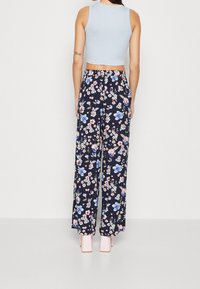 Person wearing light blue sleeveless cropped top and high-waist navy blue wide-leg pants with colorful floral print, standing facing away.